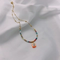 Detail of bohemian gold chain necklace with colorful faceted beads and orange enamel pendant - Orange