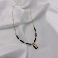 Detail of gold chain necklace with black beads and rectangular crystal pendant on silk - Black