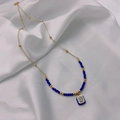 Detail of gold chain necklace featuring dark blue beads and a blue enamel crystal pendant - Blue
