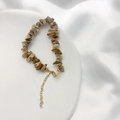 Detailopname van natuursteen armband met vergulde sluiting op een witte zijden ondergrond - Prentsteen Armband (17+5cm)