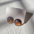 Detail van de amberkleurige hars hart oorbellen met goudstof op display kaart - Rond
