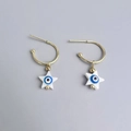 Detail of gold C-shaped earrings featuring white star charms with blue evil eye accents - Pentagram