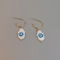 Macro view of gold Hamsa shell earrings with blue evil eye detail on grey background - Hamsa Hand