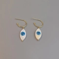 Close-up of golden evil eye drop earrings with white shell inlay and blue accents - Marquise