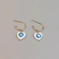 Close-up of golden heart earrings with blue evil eye enamel charms on grey background - Heart