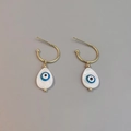 Macro shot of gold C-shaped earrings with white shell drop and blue evil eye detail - Water Drop