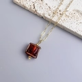 Detailed close-up of 18K gold-plated chain with square red glass pendant on white stone - Gold-Red