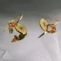 Detail von goldenen Teufelsauge-Ohrringen mit orangefarbener Opalperle auf Reflexionsfläche - Runder Teufelsauge-Stil (DE103-PN099)