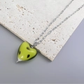 Detailed view of yellow hand-painted heart pendant on a silver-tone chain over stone - Steel Green Texture