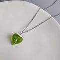 Détail du pendentif coeur en verre vert avec motifs floraux sur une fine chaîne argentée - Acier-Vert