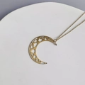 Dettaglio di un ciondolo a mezzaluna dorato con motivi a stella traforati ed eleganti - Verticale / Oro