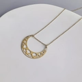 Dettaglio macro di un ciondolo a mezzaluna dorato traforato con motivi intricati - Orizzontale / Oro