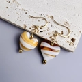 Close-up of heart-shaped resin earrings with striped patterns on a minimalist stone base - Gold and Coffee