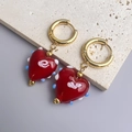 Gros plan de boucles d'oreilles cœur en verre avec spirales roses sur pierre texturée - Or-Rouge