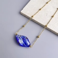 Dettaglio del ciondolo in vetro blu intenso irregolare su catena in acciaio dorato 18K - Oro-Blu Profondo
