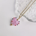 Detailopname van een hartvormige roze glazen hanger aan een gouden ketting met kralen - Harthanger (Gouden Ketting) / Goud-Roze