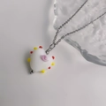Detail van zoete hartvormige geglazuurde hanger met roze krullen en kleurrijke kralen - Staal-Wit