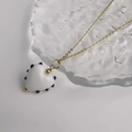 Gros plan d'un pendentif cœur en verre à pois noirs sur une chaîne dorée fine - Or-Blanc
