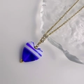 Detaillierte Makroaufnahme des blau-weiß gestreiften Glas-Herzanhängers an einer Goldkette - Gold-Blau