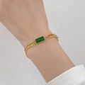Dettaglio del bracciale a doppia catena dorata con una pietra rettangolare verde al polso - Bracciale