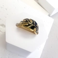 Macro detail of gold palm leaf ring with dark blue enamel inlay on a white stand - Palm Leaf