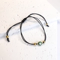 Dettaglio del bracciale in corda nera intrecciata con occhio di Allah verde e oro - Nero Verde