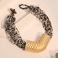 Detailopname van de meerlaagse kralenketting met een getextureerde goudkleurige hanger - Zwart & Wit