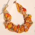 Details einer Ethno-Boho-Kette mit stoffumwickelten Perlen und Holzknopfverschluss - Gelb