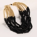 Detailed close-up of bohemian layered necklace with gold and black beads on white surface - Black