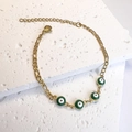 Dettaglio di bracciale dorato con ciondoli occhio di Allah su una pietra materica - Verde