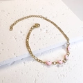 Detail of gold Figaro chain bracelet with pink evil eye enamel charms on stone surface - Pink