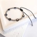 Detail of hand-woven evil eye bead bracelet with silver beads on a textured white stone - Steel-Black