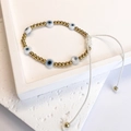 Detail of adjustable evil eye bead bracelet with gold accents and white woven string - Gold-White