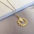 Macro detail of sunburst pendant with white oval gemstone on a golden cross chain - Gold
