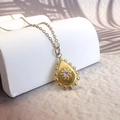 Detail of drop-shaped gold starburst pendant with crystal on geometric pedestal - Water Drop Style (DN239-0010)
