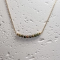 Detailopname van Unakite natuurstenen aan een gouden ketting op een wit stenen oppervlak - Unakiet