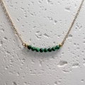 Detailopname van negen groene malachiet kralen aan een gouden ketting op steen - Malachiet
