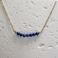 Macro view of gold chain necklace featuring seven blue lapis lazuli beads on stone surface - Lapis Lazuli