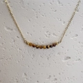 Macro shot of tiger eye beads on a thin gold chain against a white stone background - Tiger's Eye