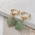 Close-up of heart-shaped green stone earrings with gold hoop on white textured stone - Green Aventurine