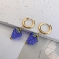 Dettaglio di orecchini a cerchio dorati con ciondoli a grappolo di uva viola - Blu