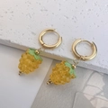 Dettaglio di orecchini in oro e acciaio al titanio con ciondoli a forma di uva in resina gialla - Giallo