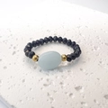 Dettaglio di un anello elastico con perline sfaccettate nere e una pietra centrale blu chiaro - Taglia unica / Nero-Blu
