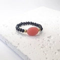 Dettaglio anello di perline nere con pietra ovale rosa su superficie in pietra bianca - Taglia unica / Nero-Rosso