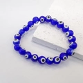 Close-up of blue glass evil eye beads elastic bracelet on a white stone background - Dark Blue