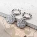 Close-up of silver hoop earrings with star-engraved hammered pendants on a stone - Star Earrings / Steel
