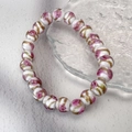 Close-up of handmade glass beads with pink rose floral patterns and gold foil texture - White