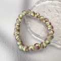 Close-up of pastel floral glass beads with gold foil accents on an elastic bracelet - Green