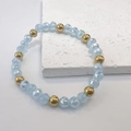 Close-up of light blue faceted beads and golden metal beads on a beaded stretch bracelet - Blue-Gold