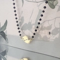 Détail du pendentif pieds de bébé dorés sur collier en perles noires à facettes fines - Empreinte